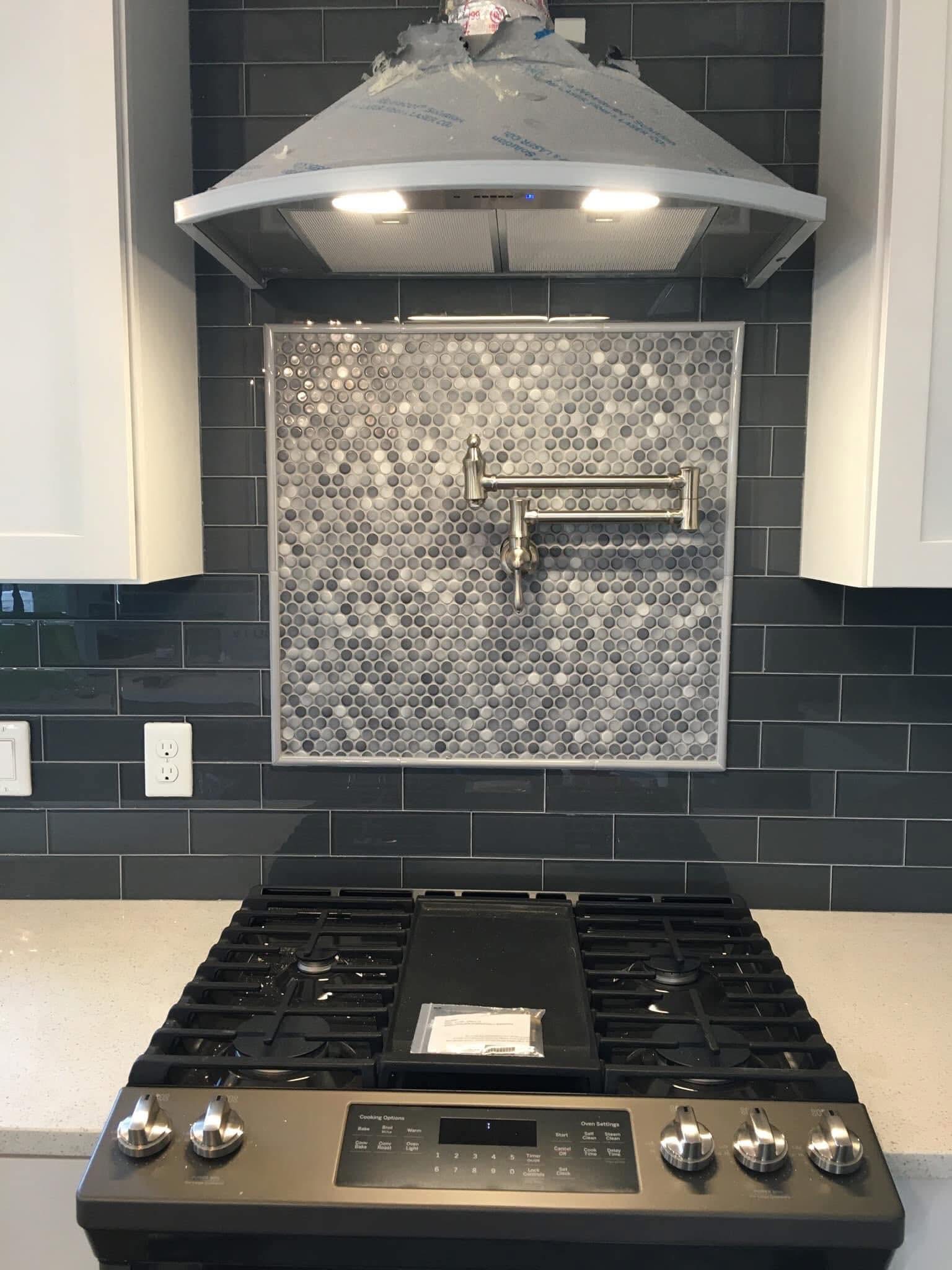 Dark tile backsplash and decorative inset behind a range hood