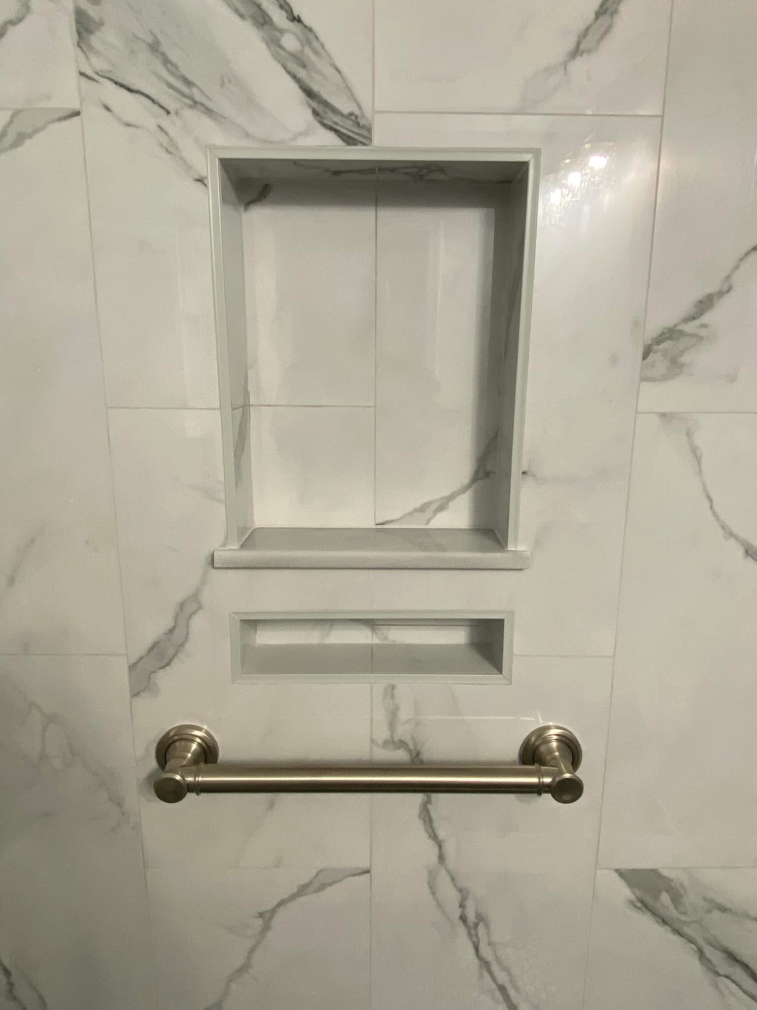 Two shower niches set in marble-look tile above a grab bar