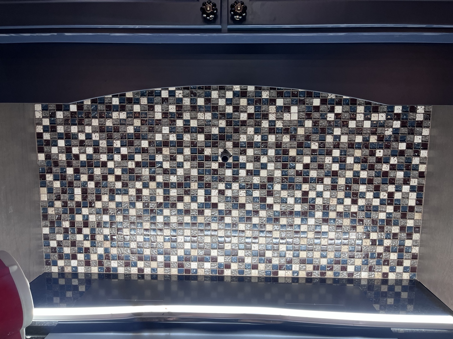 Mosaic tile backsplash beneath a dark cabinet