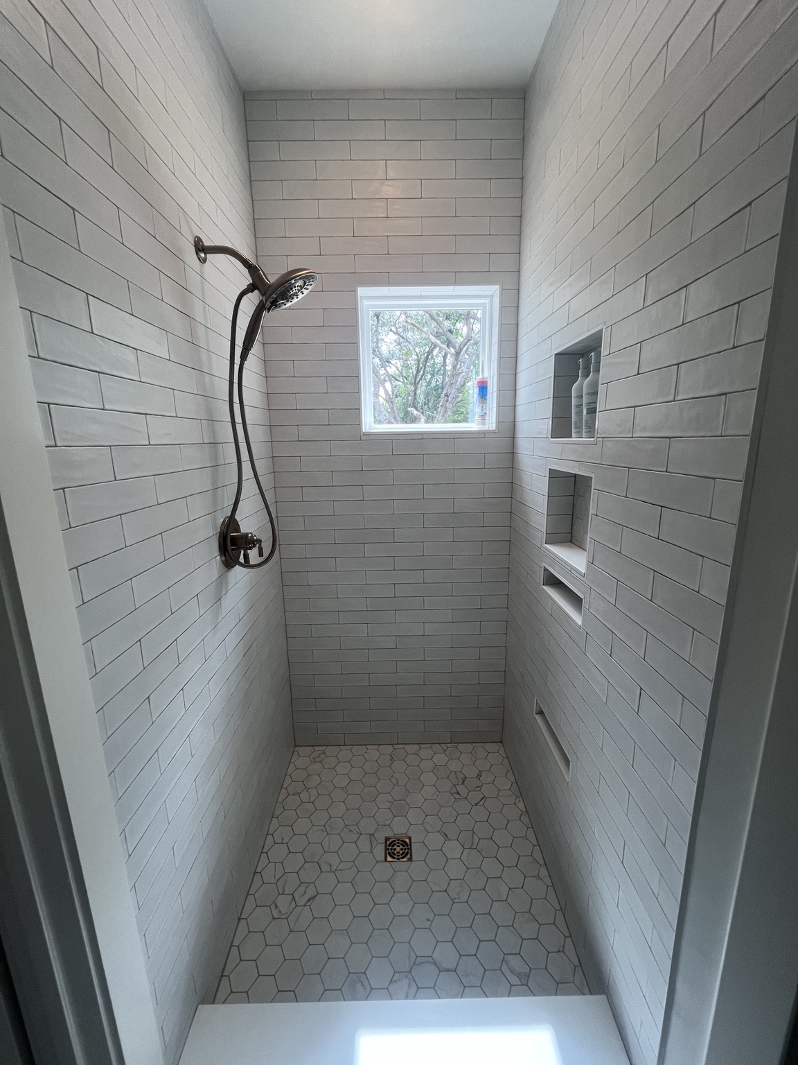 Long shower with gray tile, niche and window